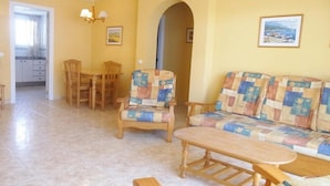 Un salon avec un canapé, des fauteuils, une table à manger et, au fond, une cuisine.