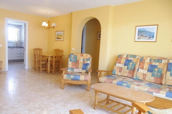 A living room with a sofa, chairs, a dining table, and a kitchen in the background.