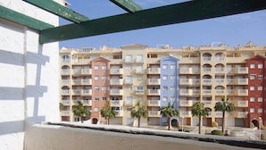 Une rangée d’immeubles résidentiels à plusieurs étages, dotés de balcons, bordée de palmiers, avec un ciel dégagé.