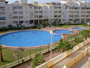 A swimming pool area with multiple pools, surrounded by a building with balconies and a well-maintained lawn. - Marinesco I and II (San Javier)