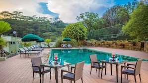 A poolside area with lounge chairs and tables, surrounded by lush greenery and a clear sky. - Hunas Falls Hotel Kandy (Kandy)