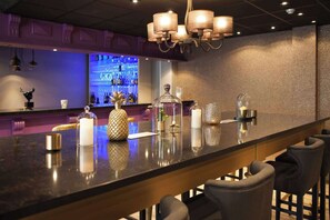 Un espace bar doté d’un long comptoir, de tabourets de bar et d’éléments décoratifs tels que des bougies et un ananas.