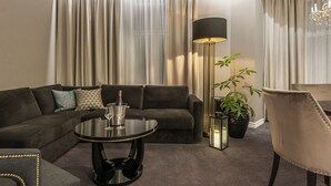 A modern living room with a dark grey sofa, a round black coffee table, a tall floor lamp, a potted plant, and a beige armchair. - Home Hotel Grand, Gjovik (Gjovik)