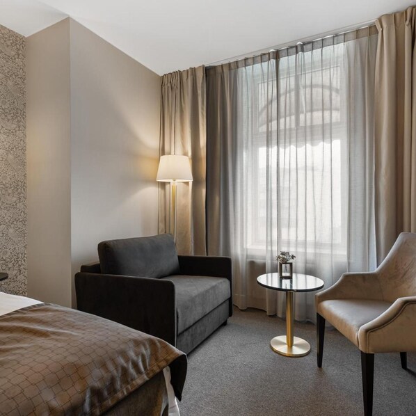Una habitación de hotel con sofá, sillón, una mesita redonda con lámpara y cama.