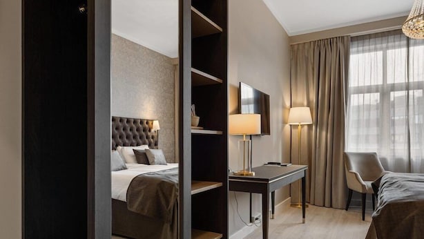 A hotel room with a bed, a desk, a chair, a TV, and a window with curtains. - Home Hotel Grand, Gjovik (Gjovik)