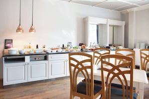 A modern kitchen with white cabinetry, a dining area with wooden chairs, and pendant lighting. - Home Hotel Grand, Gjovik (Gjovik)