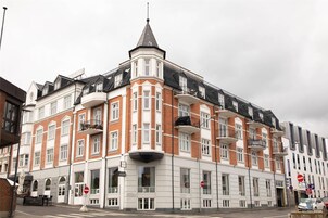 Un edificio en esquina con una torre destacada, múltiples ventanas y un letrero que indica un restaurante.