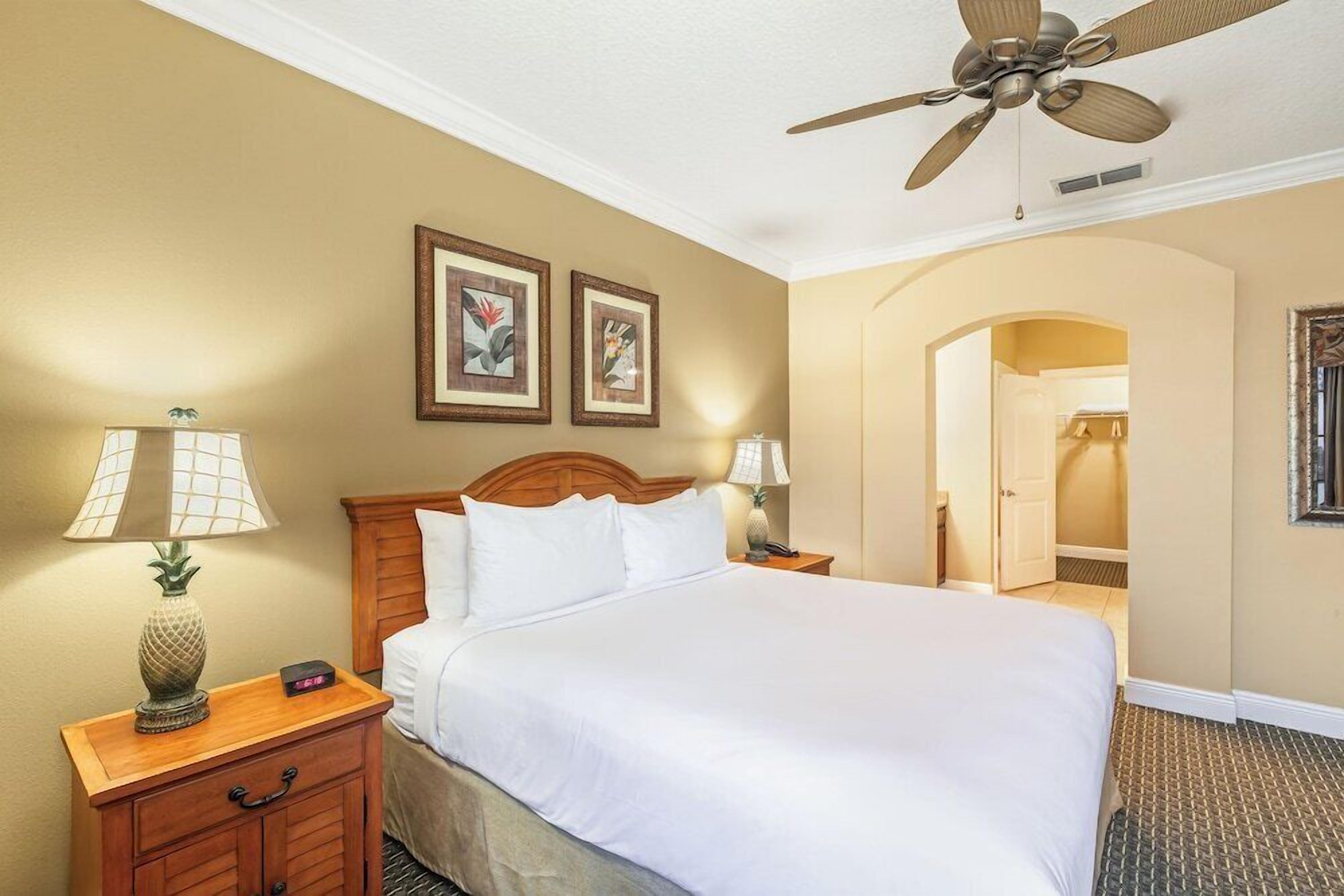 A hotel room with a bed, nightstands, a ceiling fan, and artwork on the walls.