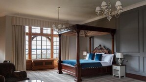 A four-poster bed with a blue bedspread, a nightstand with a lamp, and a view of the outdoors through large windows. - Murrayshall Country Estate (Perth)