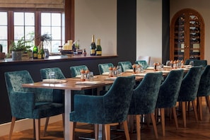 A dining area with a long table, teal chairs, and a wine rack in the background. - Murrayshall Country Estate (Perth)