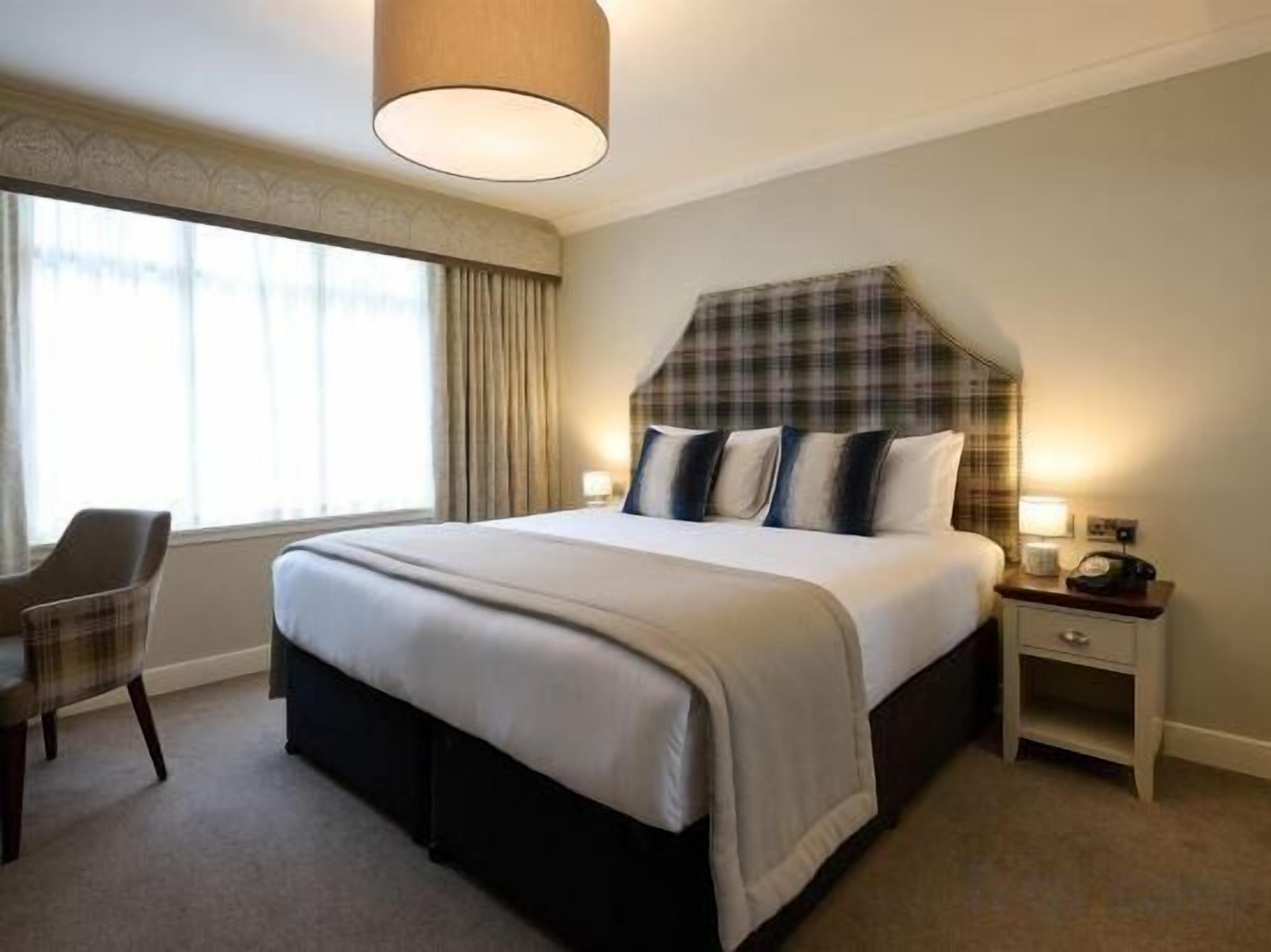 Een hotelkamer met een groot bed, een stoel, een nachtkastje en een raam met gordijnen.