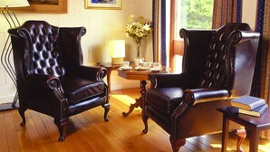 A room with two leather armchairs, a wooden coffee table, a lamp, a vase with flowers, and a painting on the wall. - Cedar Lodge Hotel and Restaurant (Carrigbyrne)
