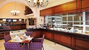 Un hall d’hôtel comprenant un comptoir d’accueil, un espace buffet et un coin salon avec des fauteuils à motifs violets.