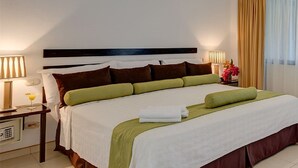 Une chambre d’hôtel avec un grand lit, deux tables de chevet, une petite table et une fenêtre avec des rideaux.