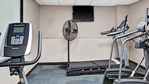 Een sportschool met loopbanden, een NordicTrack hometrainer en een staanventilator.