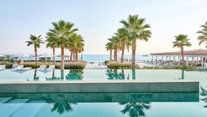 A pool area with palm trees, lounge chairs, and a view of the ocean. - Domes Noruz Kassandra - Adults-only (Kassandra)