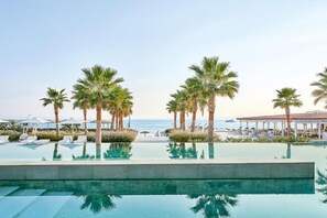 A pool area with palm trees, lounge chairs, and a view of the ocean. - Domes Noruz Kassandra - Adults-only (Kassandra)