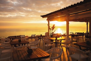 An outdoor seating area with tables and chairs, overlooking a body of water during sunset. - Domes Noruz Kassandra - Adults-only (Kassandra)