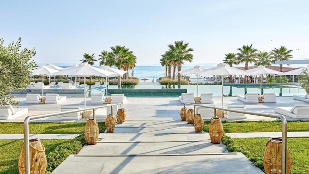 A resort pool area with white lounge chairs, palm trees, and a clear view of the ocean. - Domes Noruz Kassandra - Adults-only (Kassandra)