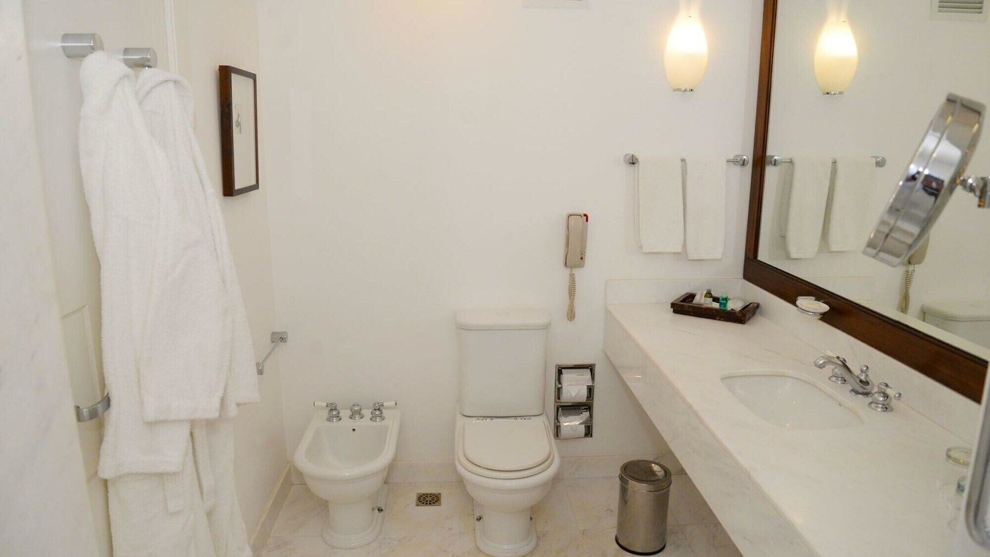 A bathroom with a bidet, toilet, sink, and a mirror.