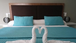 Hotellihuone, jossa on suuri sänky, kaksi samanlaista tyynyä ja koristeellinen joutsen, joka on tehty pyyhkeistä.