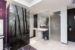 Ein modernes Badezimmer mit großem Spiegel, weißem Waschbecken und einer Duschkabine aus Glas.