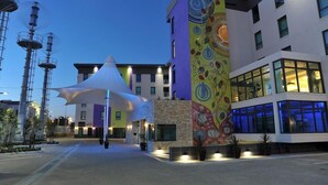 A modern hotel with a colorful mural, a white canopy structure, and a well-lit entrance area. - Hotel Verde Cape Town Airport (Cape Town)