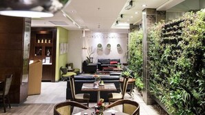 A modern dining area with a long table and chairs, a green wall with plants, and a seating area with sofas and a coffee table. - Hotel Verde Cape Town Airport (Cape Town)
