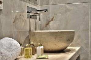 A bathroom with a large marble sink, a chrome faucet, and various toiletries on the counter. - Elia Zampeliou - Adults Only (Chania)