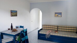 A room with a dining table, a sofa, and two framed pictures on the walls. - Ostria Seaside Studios and Apartments (Chios)
