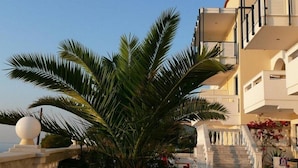 A multi-story building with a balcony, a palm tree, and a staircase leading to the entrance. - Ostria Seaside Studios and Apartments (Chios)