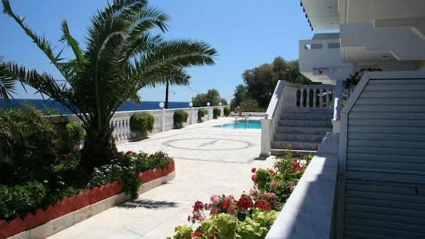 A pool area with a palm tree, a circular pathway, and a view of the sea. - Ostria Seaside Studios and Apartments (Chios)