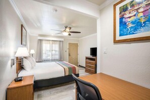 A hotel room with a bed, a desk, a chair, a television, and a ceiling fan. - Rodeway Inn at Morro Bay (Morro Bay)