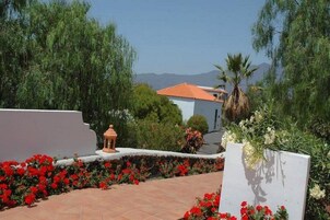 Un jardín con flores rojas, un muro blanco y un edificio con tejado rojo.