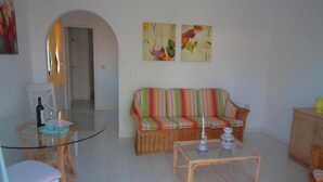 A living room with a striped sofa, a glass coffee table, and a dining table with chairs. - La Plantacion Bungalows (Los Llanos de Aridane)