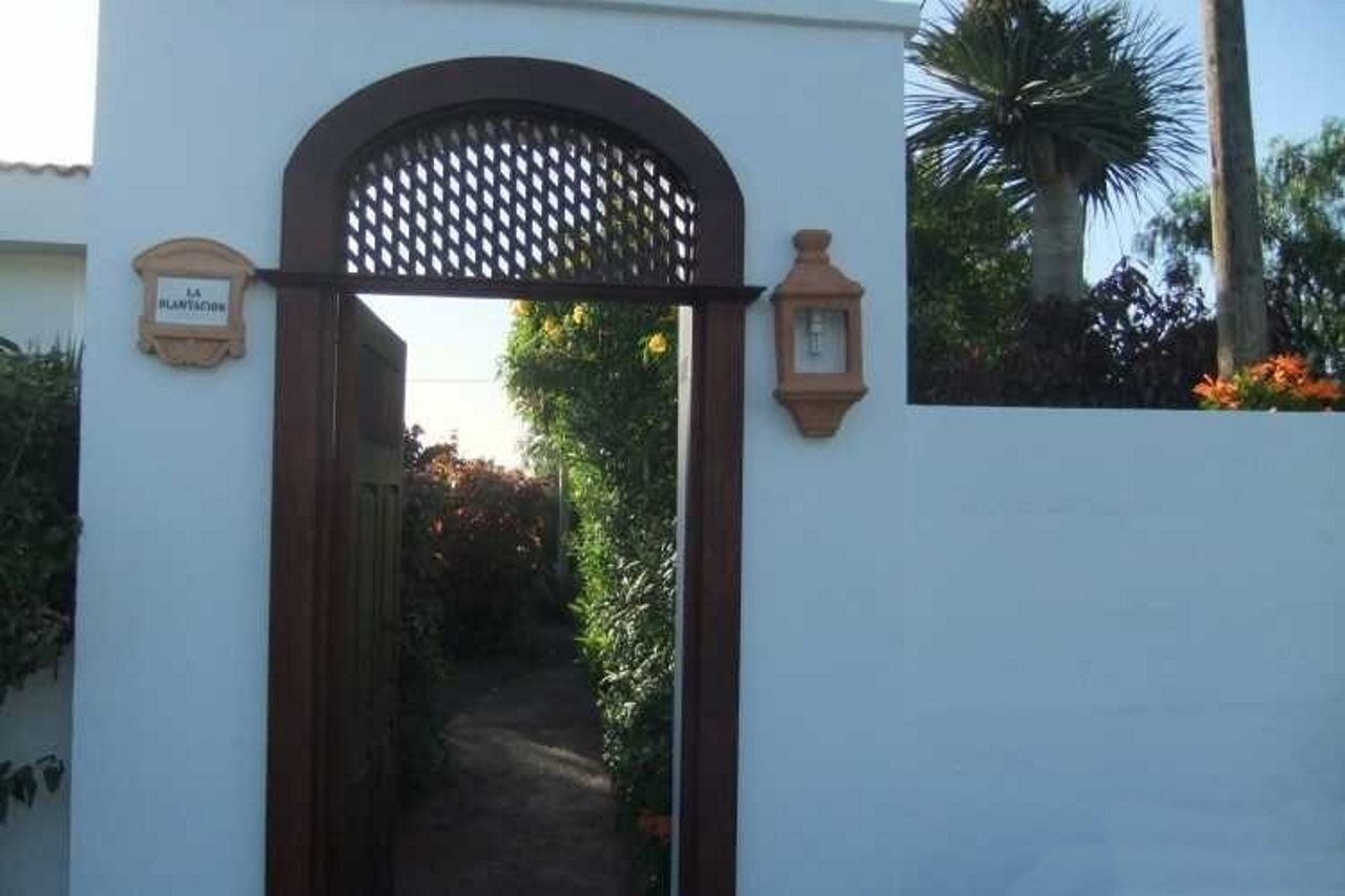 A gated entrance with a sign, a pathway leading into a garden, and a wall-mounted light fixture.