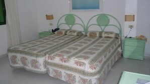 A bedroom with a double bed, green metal headboard, floral bedspread, two nightstands, and a framed picture on the wall. - La Plantacion Bungalows (Los Llanos de Aridane)