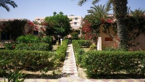 A pathway leading to a building with multiple windows, surrounded by lush greenery and palm trees. - Oasis Marine (Zarzis)