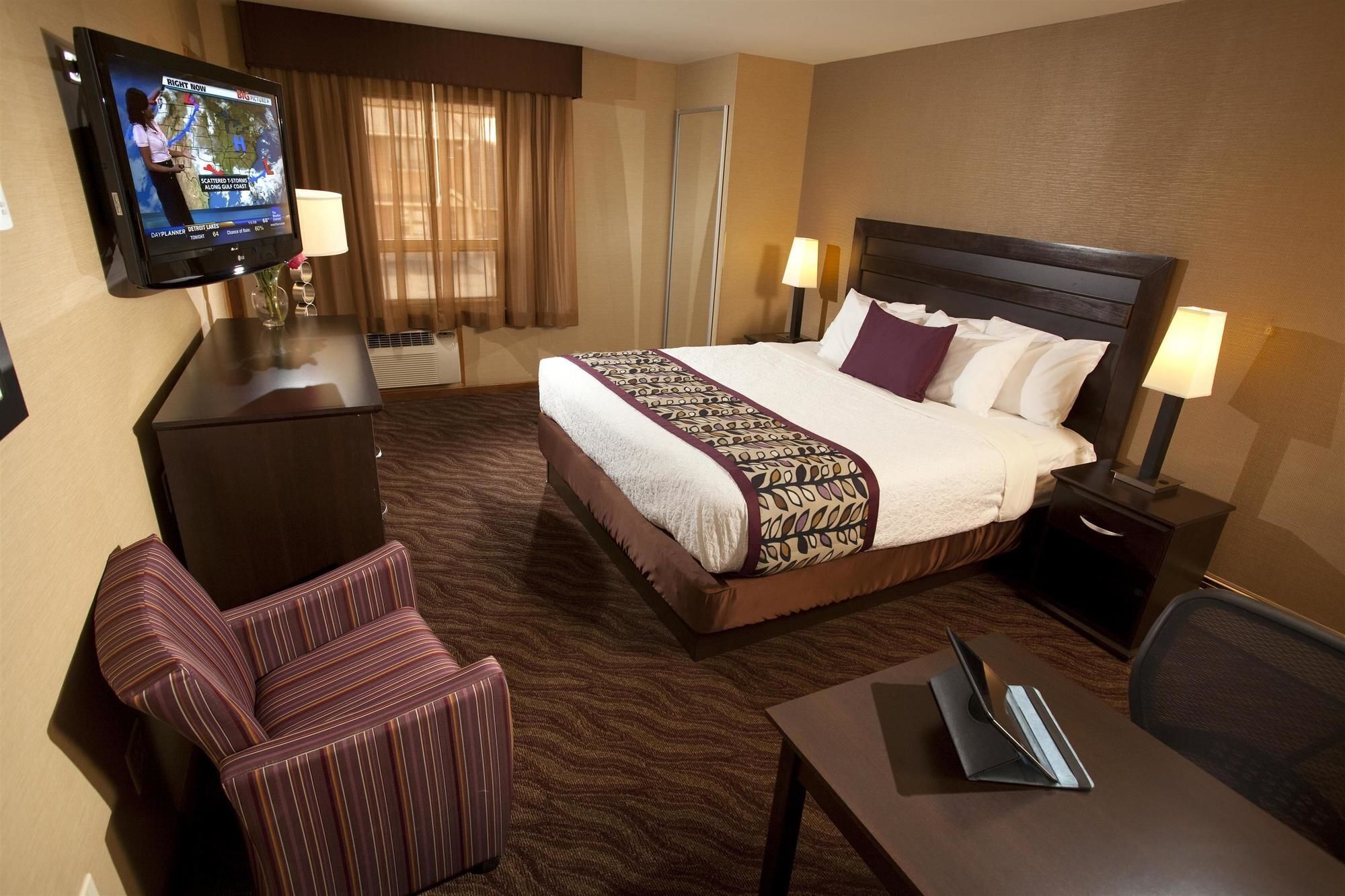 A hotel room with a large bed, a desk, a chair, a TV, and a window with curtains.