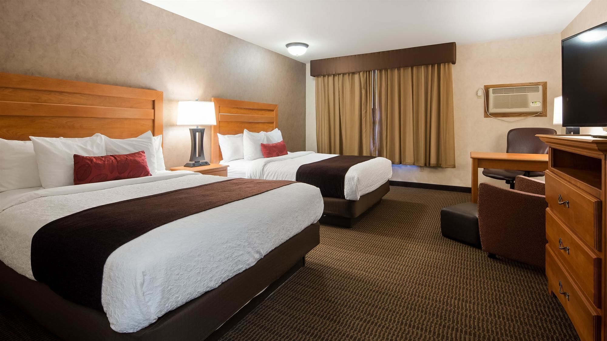 A hotel room with two beds, a desk, a chair, a dresser, and a television.