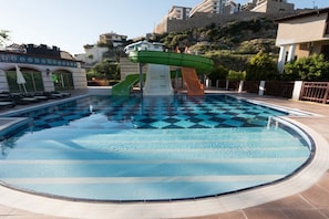 A swimming pool with a checkered pattern, a water slide, and a view of buildings in the background. - NOX INN Club Hotel (Alanya)