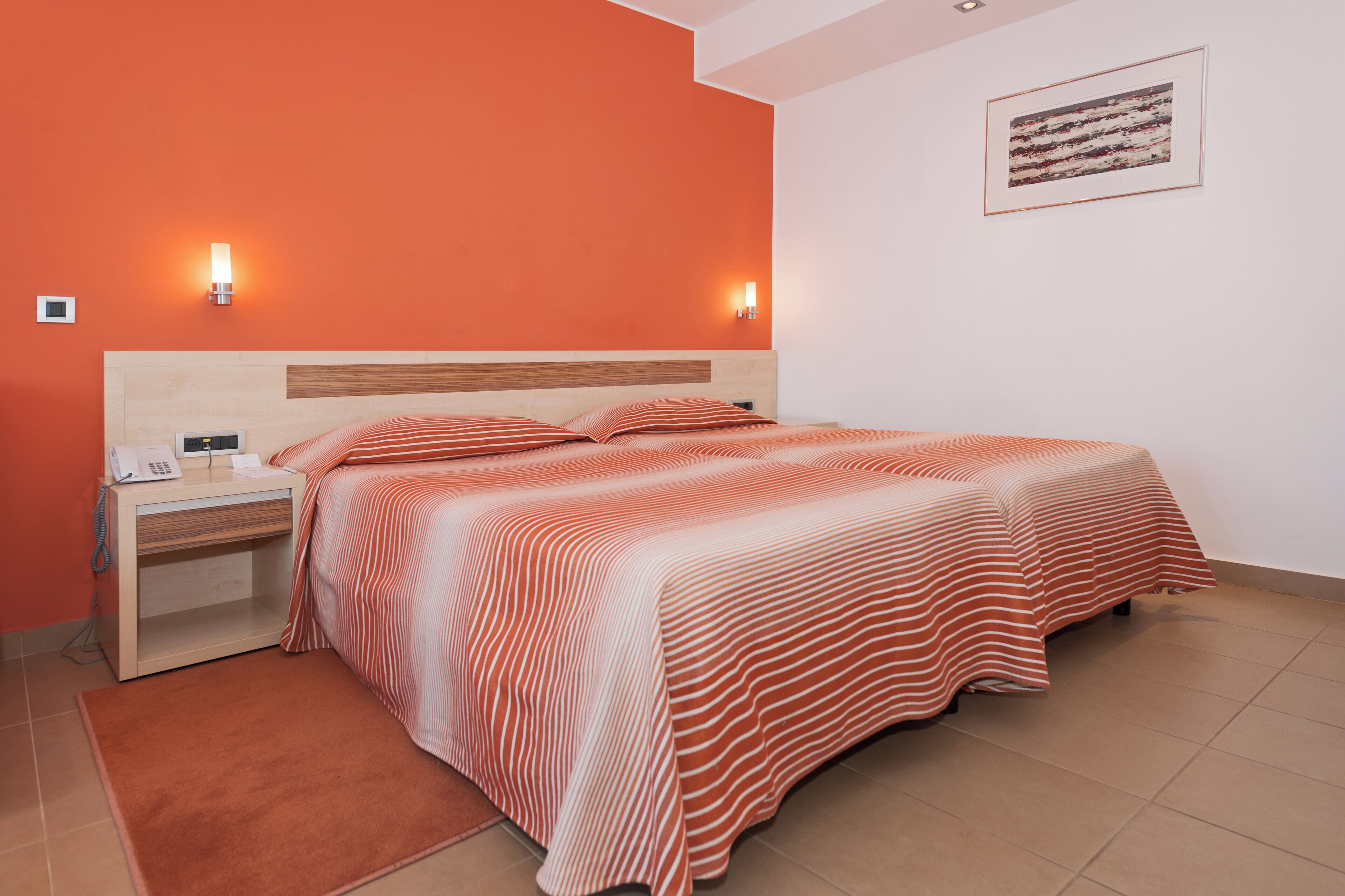 Una cama bien hecha con ropa de cama a rayas, una mesita de noche con un teléfono y dos lámparas de pared.