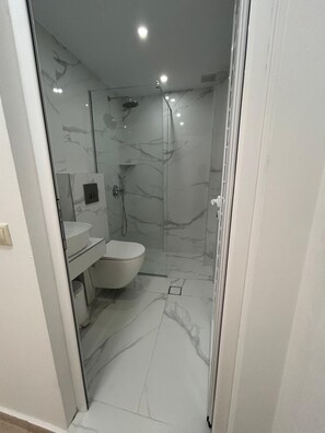 A modern bathroom with a glass-enclosed shower, a white toilet, and a marble-tiled floor. - Comfort Vaggelis Studios (Hersonissos)