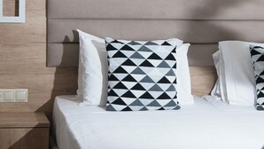 A neatly made bed with white bedding and a geometric patterned pillow. - Comfort Vaggelis Studios (Hersonissos)
