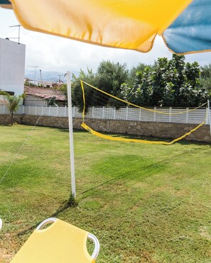 A volleyball net set up in a grassy area with a white fence and trees in the background. - Comfort Vaggelis Studios (Hersonissos)