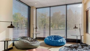 A modern room with large windows, a blue bean bag chair, a grey bean bag, and a small table with a lamp. - The Capitol Hotel, Ascend Hotel Collection (Hartford)