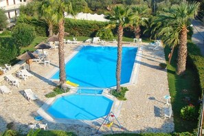 A swimming pool with two separate sections, surrounded by palm trees and lounge chairs. - Gerekos Apartments (Corfu)