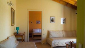 A room with two beds, a small table, a chair, and a door leading to another room. - Gerekos Apartments (Corfu)