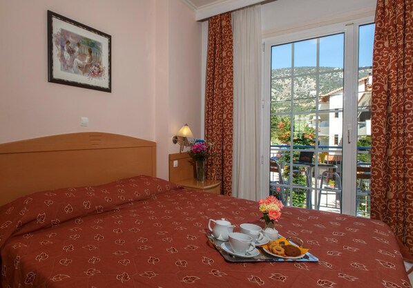 A hotel room with a bed, a bedside table with a lamp, a framed picture on the wall, and a balcony with a view of the landscape. - Tolo Tolo (Nafplio)
