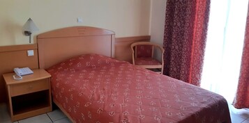 Una habitación de hotel con una cama, una mesita de noche con un teléfono, una silla y una lámpara.
